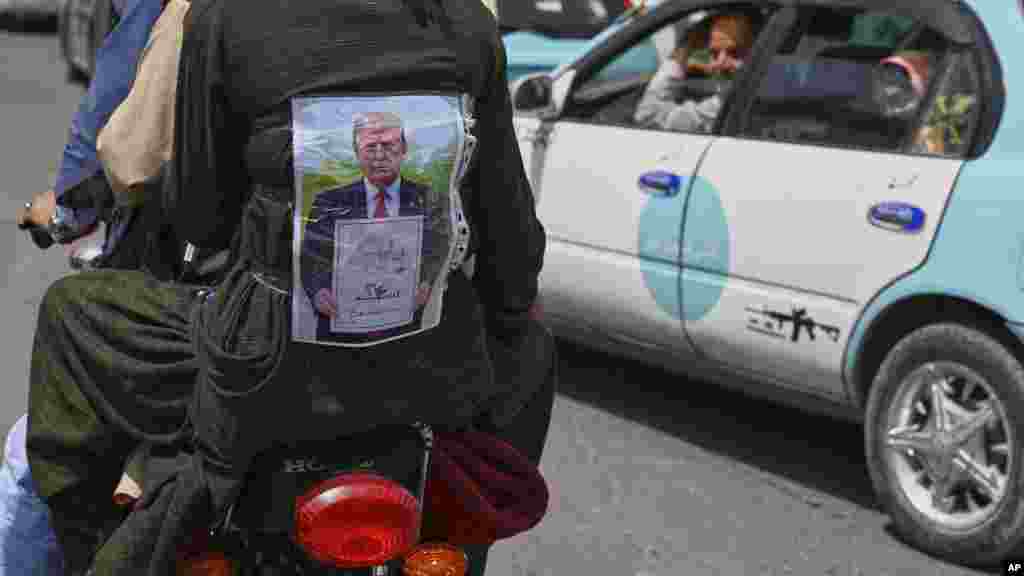 Egy férfi a pólóján Donald Trump amerikai elnök képével, amint egy papírt tart a kezében, rajta a tálibok visszatérésének dátumával és pashtu nyelven „Szökésünk napja” felirattal