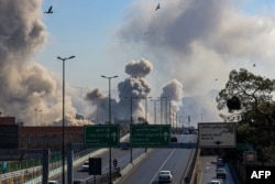 Коли се движат по път в иранската столица Техеран на фона на множество стълбове дим след въздушни атаки, 5 март 2026 г.