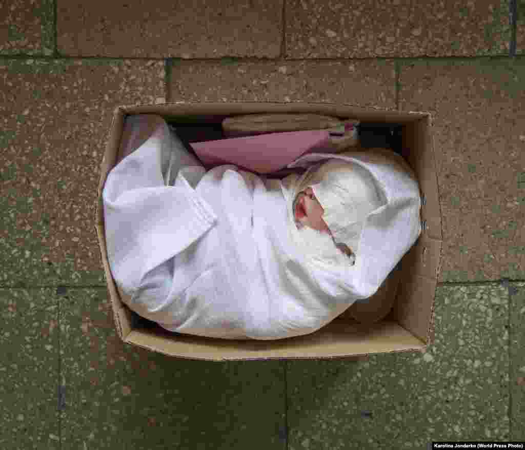 Karolina Jonderko második helyezést érő képe az Újjászületett című sorozat része. A képen egy gondosan összekészített csomag látható, egy élethű újszülött babával, születési anyakönyvi kivonattal és babaholmikkal Lengyelországban 2015. április 29-én.&nbsp;