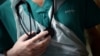 A junior doctor, wearing gloves holds his stethoscope during a patient visit on Ward C22 at the Royal Blackburn Teaching Hospital in Blackburn