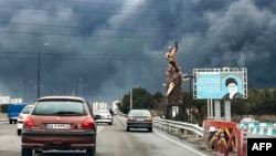 Чорний дим у небі Тегерана, авто рухаються повз статую військового меморіалу та білборд із зображенням покійного верховного лідера Ірану аятоли Алі Хаменеї. 8 березня 2026 року