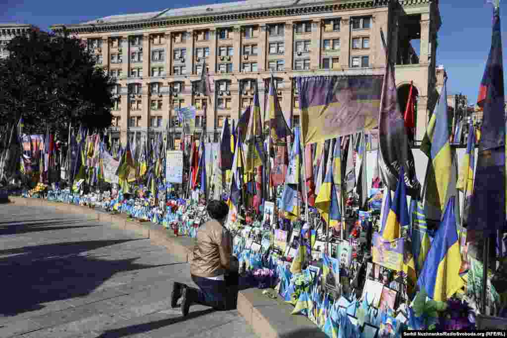 Мати стоїть на колінах біля фото свого сина на Меморіалі з прапорців на честь загиблих захисників України. Київ, 1 жовтня 2026 року