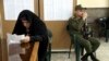 A voter fills out her ballot in the parliamentary elections as a soldier guards a polling station in Tehran, February 21, 2020