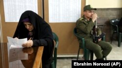 A voter fills out her ballot in the parliamentary elections as a soldier guards a polling station in Tehran, February 21, 2020