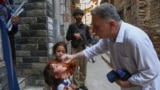 A health worker administers a polio vaccine to a child as a police officer stands guard in a neighborhood in Peshawar in Pakistan's restive Balochistan Province. 