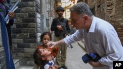 A health worker administers a polio vaccine to a child as a police officer stands guard in a neighborhood in Peshawar in Pakistan's restive Balochistan Province. 