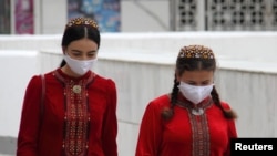 Women wearing protective face masks walk along the street in Ashgabat.