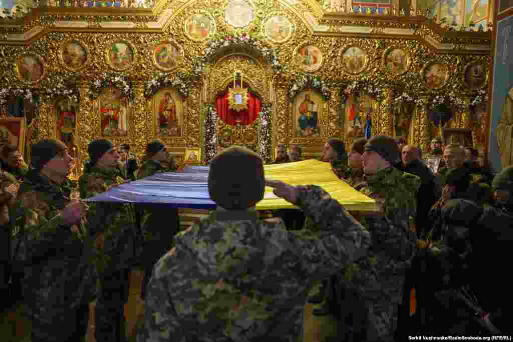 Побратими накривають труну українським прапором під час прощання у Михайлівському золотоверхому соборі.&nbsp; &laquo;Сьогодні мені вручили прапор, яким була накрита твоя труна. Сьогодні всі кидали в твою могилу землю, а я поклала в неї своє серце. Люблю тебе. Ми тебе любимо. І любитимемо завжди&raquo;, &ndash; написала у своїй сторінці у фейсбуці дружина загиблого військового Анастасія Федченко 