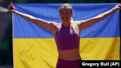 Viktoriya Tkachuk of Ukraine poses for a teammate with a flag signed by the Ukrainian rock band The Hardkiss as she trains before the World Athletics Championships in Eugene, Oregon, on July 14.