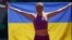 Viktoriya Tkachuk of Ukraine poses for a teammate with a flag signed by the Ukrainian rock band The Hardkiss as she trains before the World Athletics Championships in Eugene, Oregon, on July 14.
