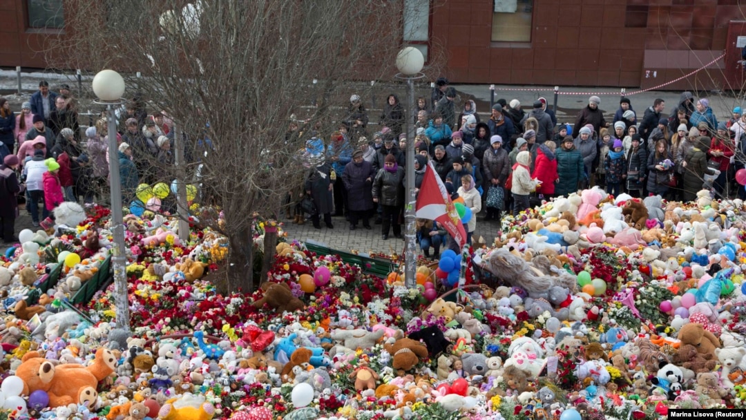 People stand near toys, flowers, balloons, and other items as they gather to commemorate the victims of a shopping mall fire on the day of national mourning in Kemerovo on March 28.