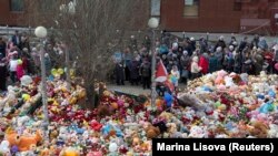 People stand near toys, flowers, balloons, and other items as they gather to commemorate the victims of a shopping mall fire on the day of national mourning in Kemerovo on March 28.