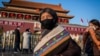 Tourists from Tibet wearing a protective mask (R) and a scarf as a mask (C) walk in front of the portrait of late communist leader Mao Zedong (back) at Tiananmen Gate in Beijing on January 23, 2020. - China is halting public transport and closing highway 