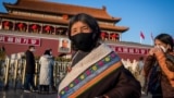 Tourists from Tibet wearing a protective mask (R) and a scarf as a mask (C) walk in front of the portrait of late communist leader Mao Zedong (back) at Tiananmen Gate in Beijing on January 23, 2020. - China is halting public transport and closing highway 