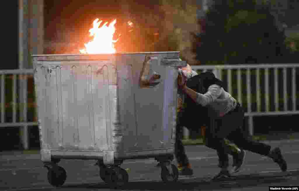 Protesters push a burning trash can towards riot police in Bishkek on October 5.