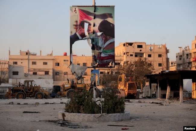 Dəməşqdə Suriyanın keçmiş prezidenti Bəşər əl-Əsəd və İranın ali lideri Əli Xamenei arasında görüşü əks etdirən cırılmış plakat.