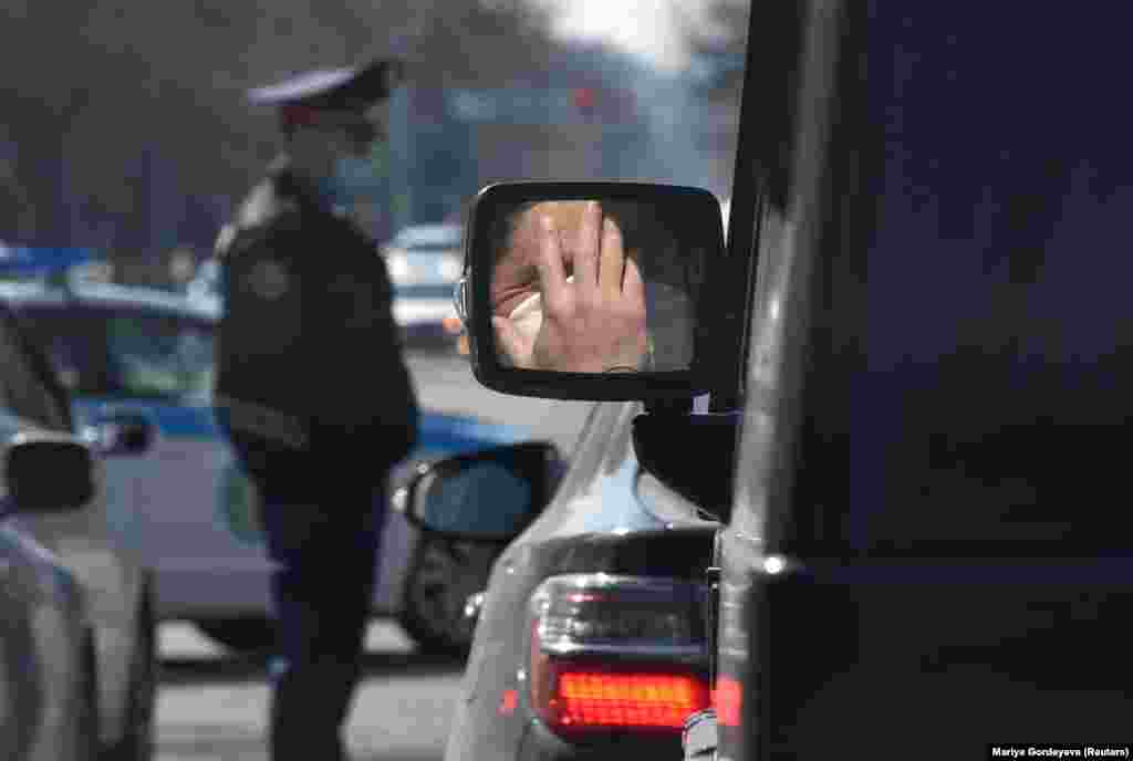 A person wearing a protective mask against the coronavirus is reflected in the side mirror of a car near a Kazakh police officer in Almaty on March 30. (Reuters/Mariya Gordeyeva)