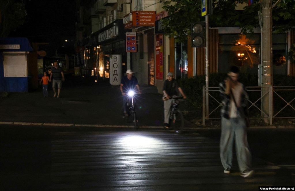 Çiklistë dhe këmbësorë në një rrugë të errësuar në Jevpatoria më 5 korrik.Kriza e energjisë elektrike në Krime, e cila po zhvillohet paralelisht me mungesat e vazhdueshme të karburantit në gjithë gadishullin, ka bërë që në disa qytete të preken shërbime jetike, si furnizimi me ujë, ndërsa shërbimi i tramvajit është pezulluar.