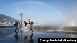 CRIMEA – People run along an embankment away from a water splash, with a rainbow seen in the background, in the Black Sea resort of Yalta, Crimea, 30Sep2021