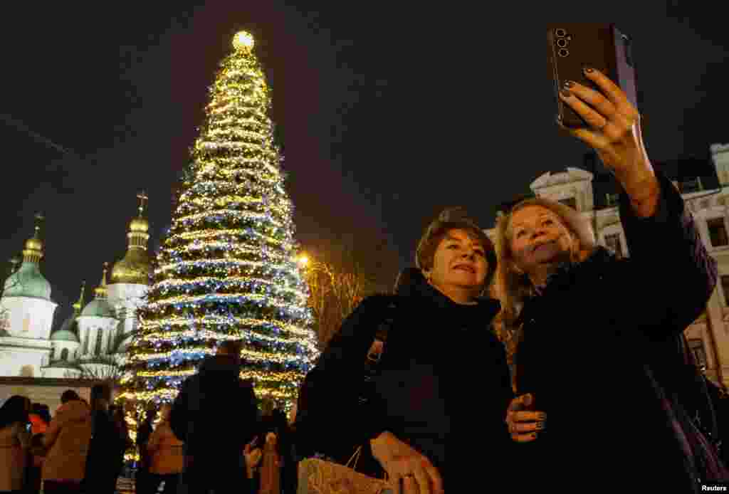 Люди фотографируются, собравшись вокруг главной рождественской елки Украины после включения ее огней перед Софийским собором в Киеве, Украина, 5 декабря 2025 года. REUTERS/Gleb Garanich