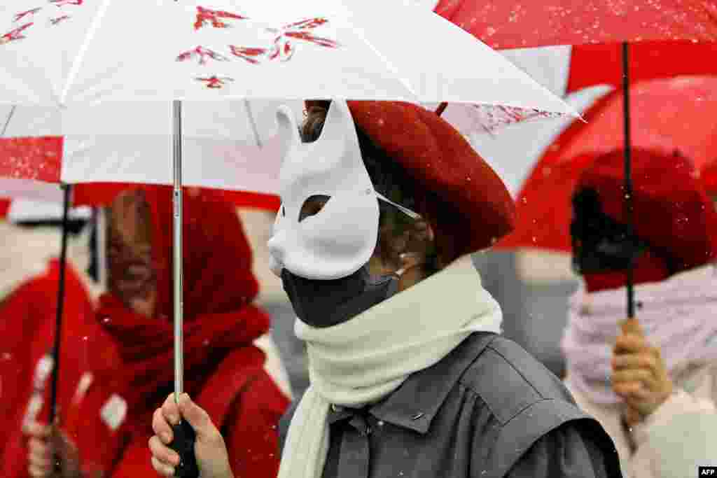 Women wearing carnival masks march under umbrellas with the colors of the former white-red-white flag of Belarus to protest against the Belarus presidential election result in Minsk on January 26. (AFP/Stringer)