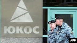 Two Russian policemen pass by the Yukos oil giant's logo during the controversial auctioning of some of the company's key assets at its headquarters in 2007. (file photo)