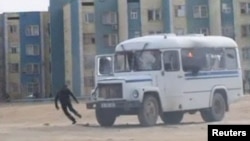 In this still image taken from video acquired by Reuters, a protester runs from a police vehicle on fire in the Kazakh town of Zhanaozen 