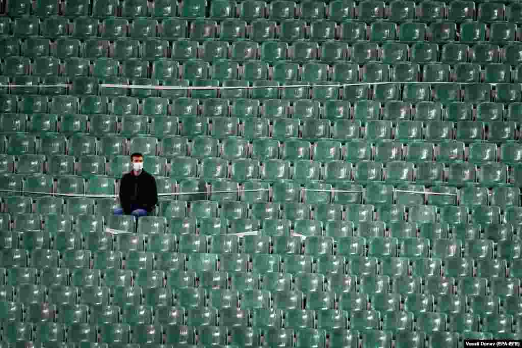 Një tifoz i futbollit, që ka vendosur maskë mbrojtëse, qëndron në një stadium të zbrazët. Ai po ndjek një ndeshje kualifikuese për Euro 2020 ndërmjet Bullgarisë dhe Hungarisë të mbajtur në Sofje më 8 tetor. (epa-EFE/Vassil Donev)