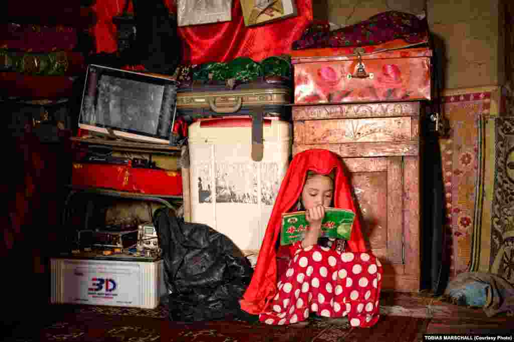 A young Pamir Kyrgyz girl does homework in the mud-brick house of a winter settlement.