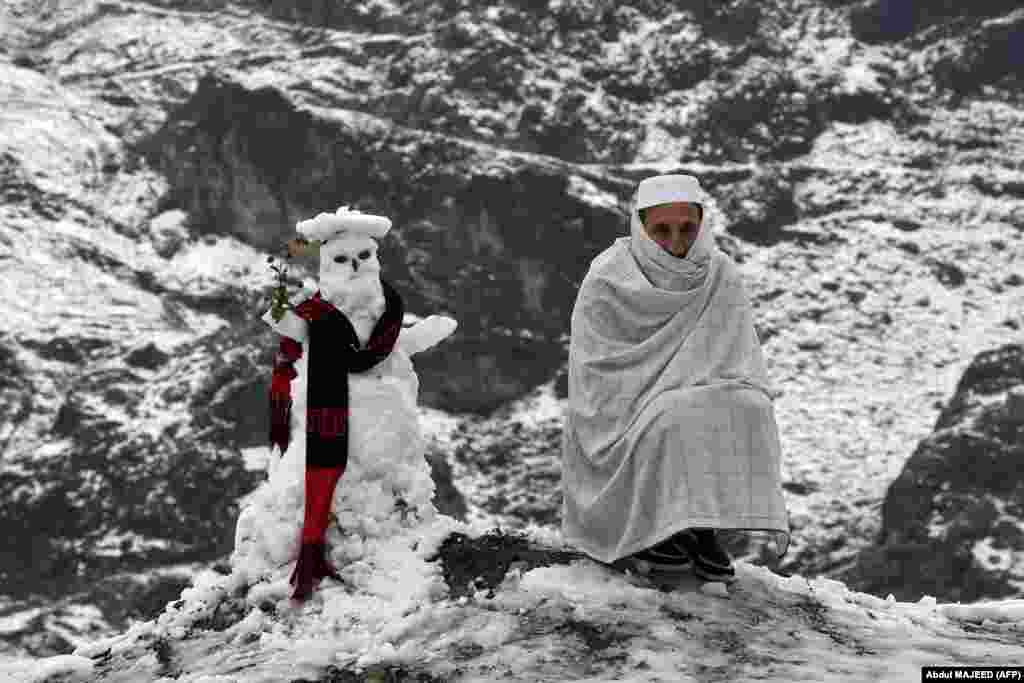 A man sits next to a snowman after the first snowfalls in Landi Kotal, Pakistan. (AFP/Abdul Majeed)