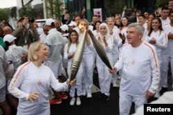 Emma Terho (s), președintele Comisiei Atleților a CIO și Thomas Bach (d), președintele Comitetului Internațional Olimpic (CIO) în timpul preluării torței din Satul Olimpic.