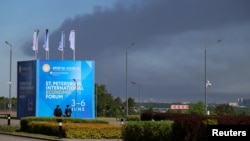 Pillars of smoke rise into the sky above Russia's St. Petersburg on June 3, behind a banner advertising the city's 29th International Economic Forum.