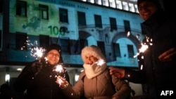 Хора празнуват посрещането на Нова година на фона на сградата на БНБ, осветена в чест на влизането на България в Еврозоната, София, 31 декември 2025 г.