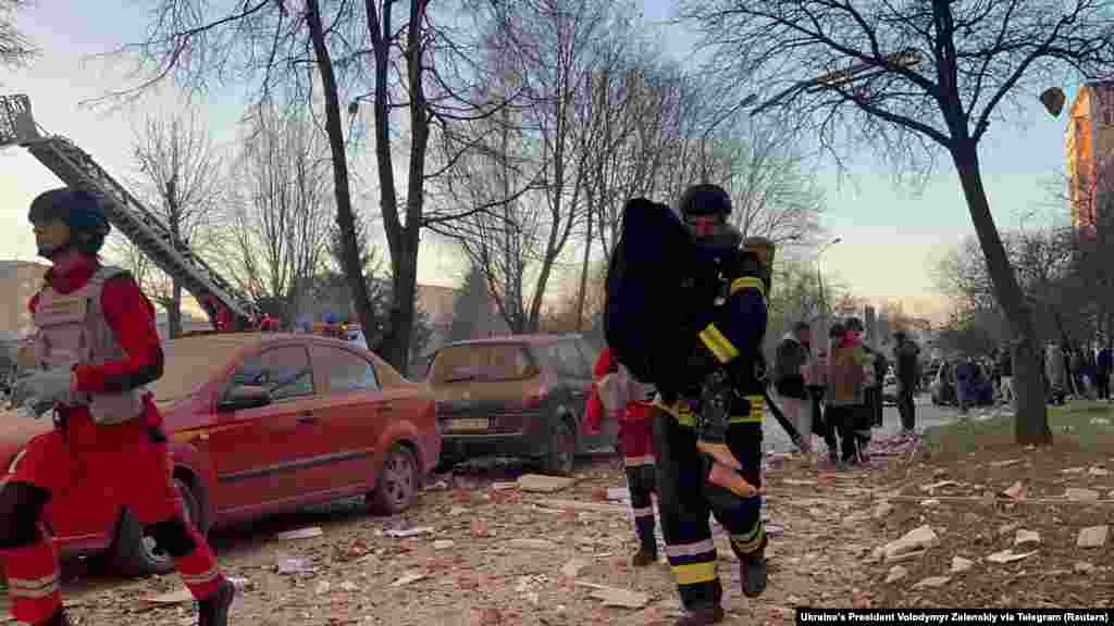 Рятувальник несе людину поруч з будинком, у який влучила російська ракета.