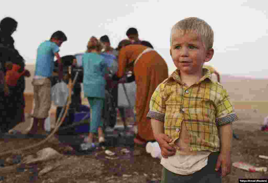 A Syrian boy stands near people using containers to collect water at the Arbat refugee camp in the northern Iraqi province of Sulaimaniyah. (Reuters/Yahya Ahmad)