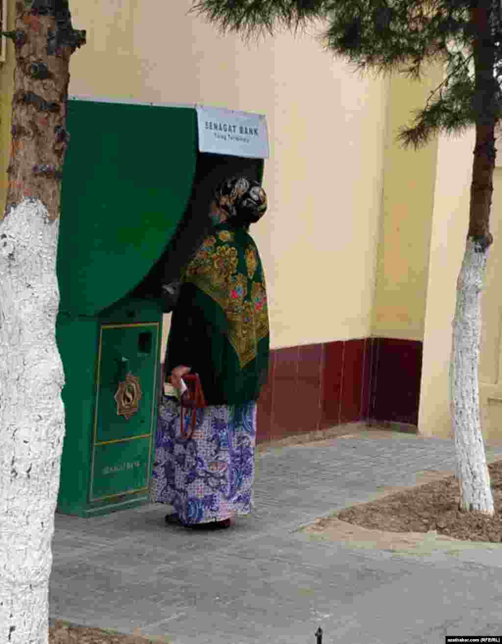 Aýal maşgala &quot;Senagat&quot; bankynyň bankomatyndan pul almaga synanyşýar. Aşgabat, mart, 2021 &nbsp;