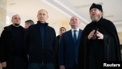 Vladimir Putin (al doilea din stânga), guvernatorul Sevastopolului, Mihail Razvojaiev (centru), și Mitropolitul Tihon (dreapta), președintele Consiliului Patriarhal pentru Cultură, vizitează un centru pentru copii din Sevastopol, Crimeea, 18 martie.