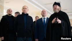 Președintele rus Vladimir Putin, însoțit de guvernatorul pro-rus al Sevastopolului, Mihail Razvozhayev, și de mitropolitul Tihon, președintele Consiliului Patriarhal pentru Cultură, vizitează un centru de artă și estetică pentru copii din Sevastopol, Crimeea, 18 martie 2023.