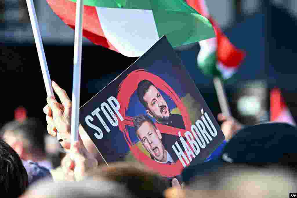 Прихильники прем’єр‑міністра Угорщини Віктора Орбана тримають національні прапори та плакат із портретами президента України Володимира Зеленського та лідера угорської опозиції Петера Мадяра з написом «Зупиніть війну» перед будівлею парламенту під час передвиборчого мітингу 15 березня