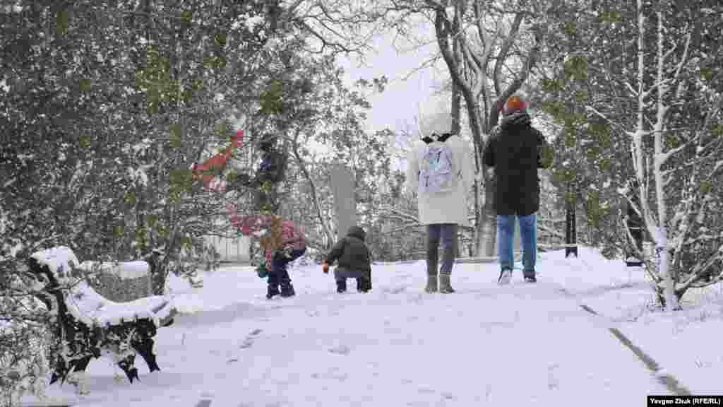 Дети играют в снежки, пока родители прогуливаются по аллее