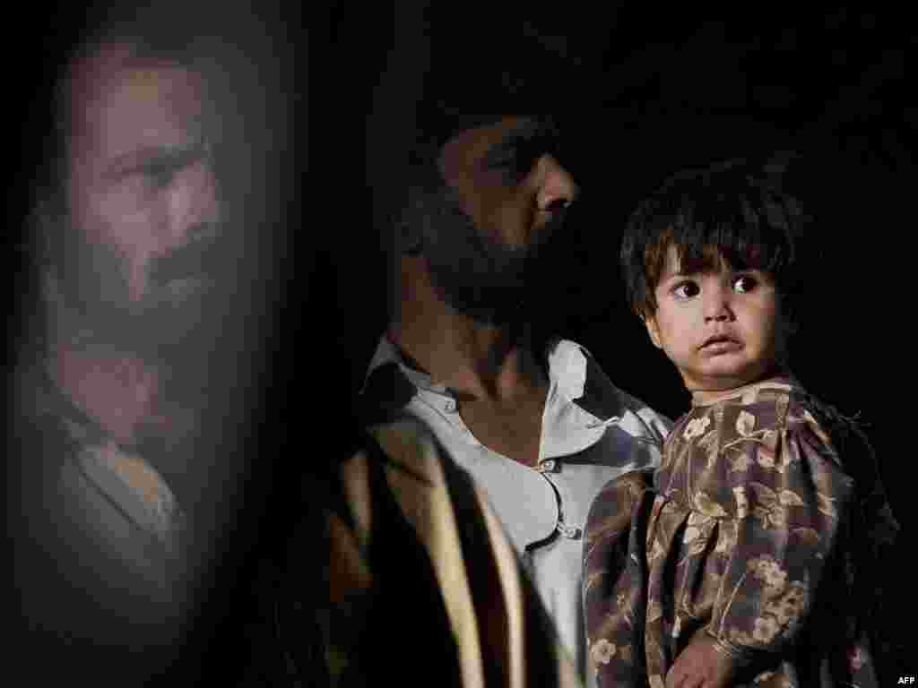 Pakistan -- A Pakistani man (C) holds a baby as another man (L) is seen behind a window car passing by in a street at sunset in Rawalpindi, on the outskirts of capital Islamabad, 22Oct2009 - PAKISTAN, Rawalpindi : A Pakistani man (C) holds a baby as another man (L) is seen behind a window car passing by in a street at sunset in Rawalpindi, on the outskirts of capital Islamabad, on October 22, 2009. The insurgency-hit country is fearing fresh attacks in a month that has left around 185 people dead as troops pressed a major offensive against Taliban networks.