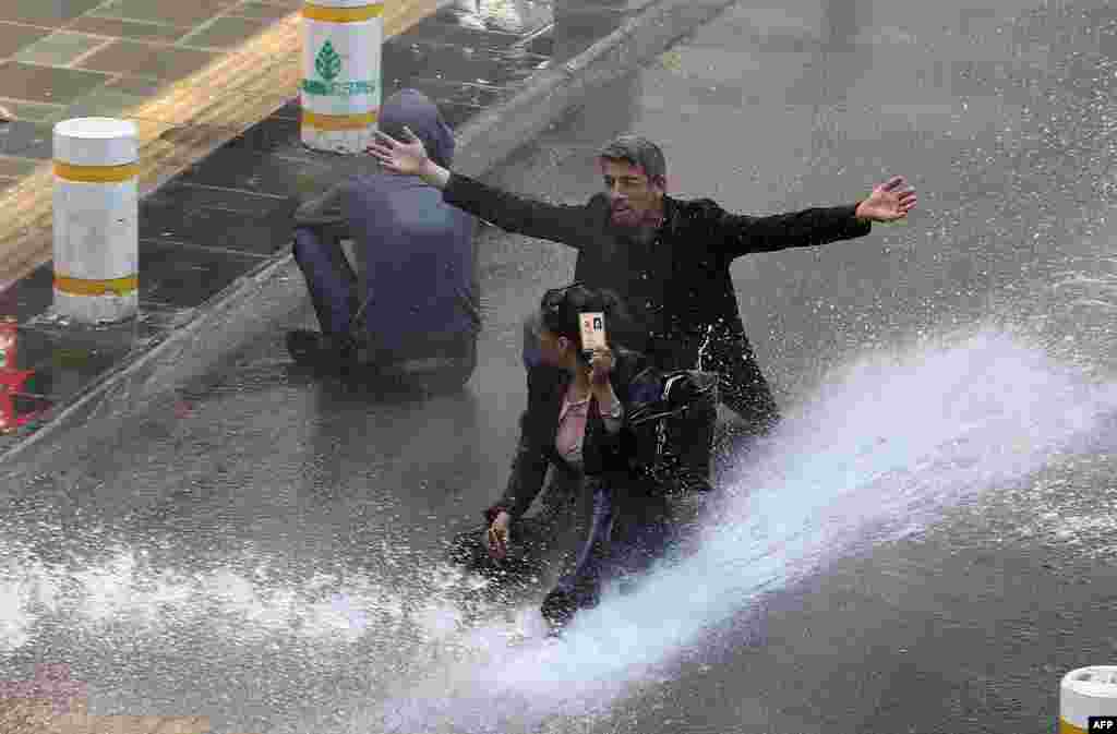 A Turkish woman shows her identity card next to another protestor as riot police use water cannon during clashes after hundreds of people tried to reach Ankara&#39;s main Kizilay Square to celebrate May Day in Ankara. (AFP/Adem Altan)