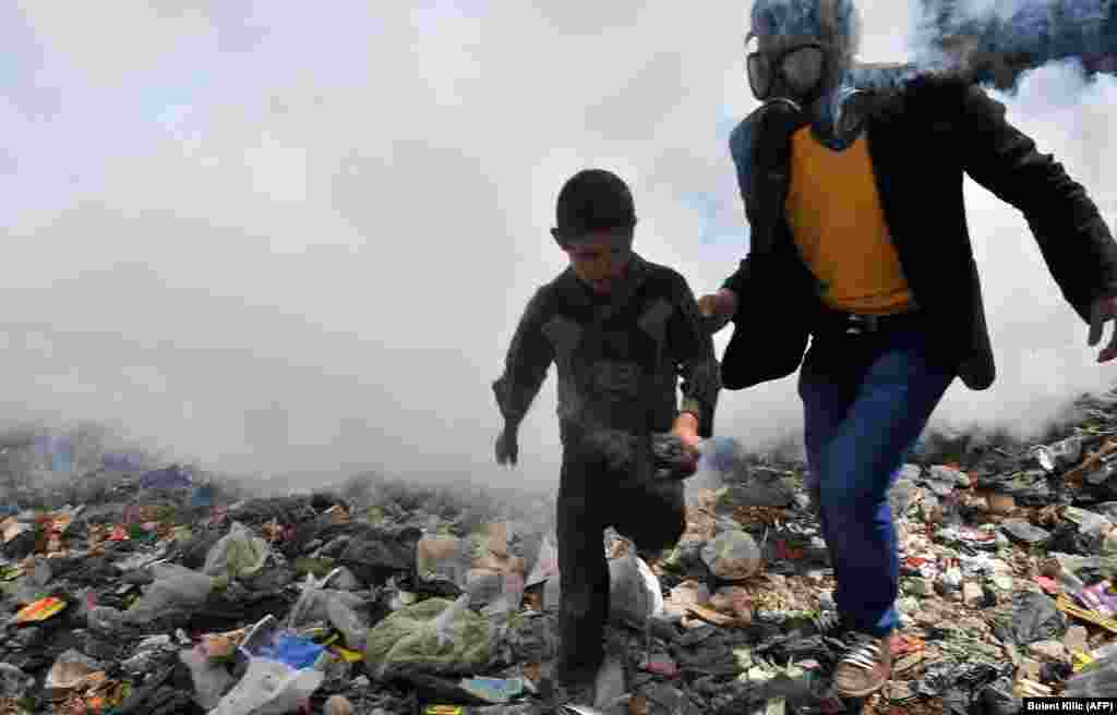 A man escorts a boy away from fumes as a street covered with uncollected garbage is fumigated in the northern Syrian city of Aleppo. (AFP/Bulent Kilic)