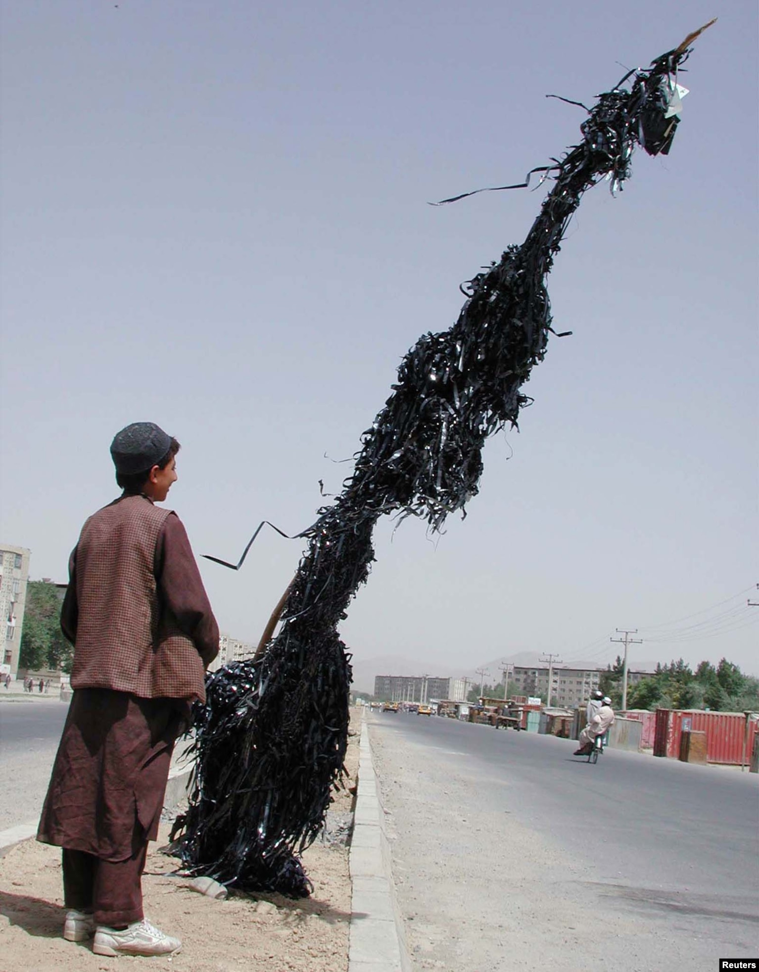 Një djalë afgan shikon një shtyllë të lidhur me shirita të videokasetave dhe audiokasetave të shkatërruara, Kabul më 2001.