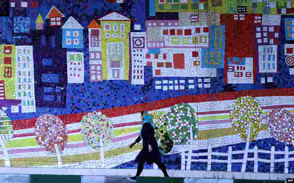 An Iranian woman walks past a mural on a street in northwest Tehran. (AFP/Atta Kenare)