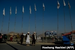 Taliban fighters walk past Taliban flags flying on poles along a street in Kabul on September 26.