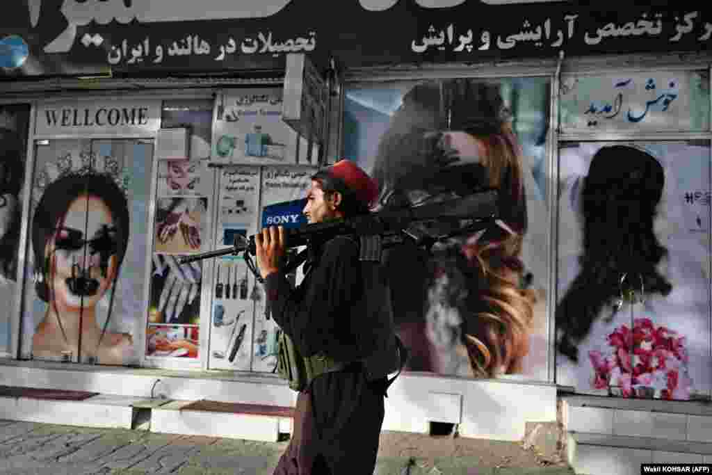 Një luftëtar taliban kalon pranë një salloni bukurie, ku imazhet e grave janë përdhosur.