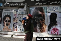 A Taliban fighter walks past a beauty salon with images of women defaced using spray paint in Shar-e Nau in Kabul.