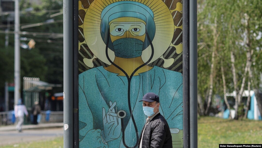 Imagine de arhivă cu un bărbat care trece pe lângă un afiș în care un medic este înfățișat într-o postură religioasă, București, România, 29 aprilie 2020.