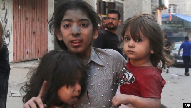 Una ragazza palestinese tiene in braccio altri due bambini dopo un attacco militare israeliano a Gaza City il 12 ottobre 2023.